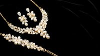 Elegant gold floral jewelry set with pearls and crystals on black background. Luxury bridal accessories including necklace and earrings for wedding ceremonies.