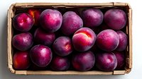 Fresh ripe purple plums in wooden crate, top view. Raw organic fruit with deep burgundy skin showing natural bloom, arranged in rustic market box.