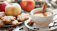 Cozy winter scene with hot spiced drink, cinnamon stick, star anise, gingerbread cookies and fresh apples on rustic wooden table.