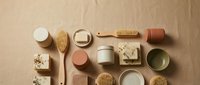 Flat lay arrangement of natural skincare and bath products including wooden brushes, ceramic containers, soap bars, and spa accessories on neutral beige background.