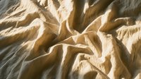 Crumpled beige fabric with natural folds and shadows, suitable for textile backgrounds, design overlays, and creative projects.