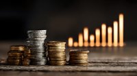 Stacks of gold and silver coins against dark background with blurred ascending graph of glowing bars, representing financial growth and investment success.