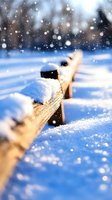 Fresh snow covering wooden fence rail against blue winter background with falling snowflakes creating magical seasonal atmosphere.