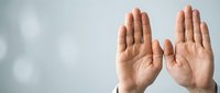 Two open palms raised upward in gesture of surrender, prayer or offering against soft gray background with copy space for text and design.