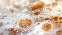 Golden water droplets on white foam surface with sparkling bubbles and warm sunlight creating luxurious spa and wellness atmosphere for relaxation concepts.