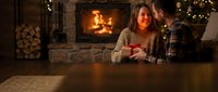 Young couple enjoying romantic evening by fireplace in cozy living room with warm lighting and festive decorations during winter holidays at home.