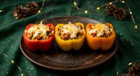 Three colorful stuffed bell peppers with melted cheese on rustic wooden plate, festive holiday dinner setting with pine cones and warm lights for cooking blogs.