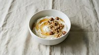 Creamy yogurt bowl topped with crunchy granola, nuts and honey drizzle on rustic linen background for healthy breakfast and wellness lifestyle content.