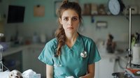 Young female medical professional in teal scrubs and stethoscope looking concerned while working in hospital setting, portraying healthcare worker stress and dedication.