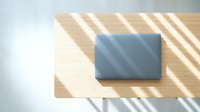 Closed laptop computer with blue-gray screen on wooden surface with diagonal window shadows, isolated on white background for design mockups and tech presentations.