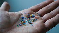 Colorful tiny microplastic particles scattered in open palm showing environmental pollution and contamination concerns for research and awareness.