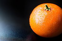 Fresh ripe orange fruit with textured peel and green stem on dark reflective surface with water droplets for healthy eating and nutrition concepts.
