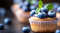 Fresh blueberry muffin topped with ripe berries and mint leaves on dark background, selective focus with natural lighting for food photography and bakery.