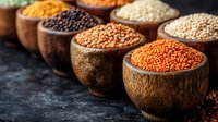 Variety of colorful lentils and legumes in wooden bowls on dark background. Raw organic pulses collection for healthy protein-rich vegetarian cooking.