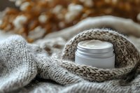 Moisturizing cream jar on cozy knitted beige sweater background with soft focus. Natural skincare and winter body care concept for beauty and spa.