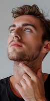 Young Caucasian male model with blue eyes looking up thoughtfully while touching chin against neutral background, wearing casual black t-shirt, studio portrait shot.