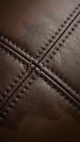 Brown leather surface with decorative cross-stitched seams showing detailed craftsmanship and texture for luxury goods and fashion accessories.