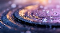 Macro photography of water drops on purple and gold metallic surface with circular pattern creating abstract background with bokeh light effect and reflections.