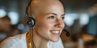 Smiling bald woman wearing headset in customer service role, working in bright office environment with blurred background.