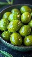 Fresh green olives with water drops in ceramic bowl on dark background, macro food photography showing texture and shine of Mediterranean appetizer.