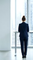 Professional businesswoman in navy suit standing at modern office window overlooking city skyline, contemplating future business opportunities and success.