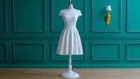 Elegant white dress on mannequin against emerald green wall with decorative molding and golden wall sconce. Classic feminine fashion display setup.
