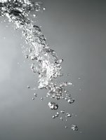 Dynamic stream of rising bubbles in crystal clear water against gray background, captured in high-speed photography showing detailed water motion and light refraction.
