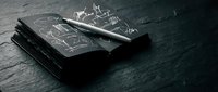 Notebook with sketched business graphs and pen on dark textured surface, suitable for corporate presentations, financial planning materials, and business strategy content.
