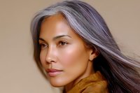 Asian woman with long silver gray hair and natural makeup wearing brown turtleneck sweater against neutral beige background, side profile portrait showing graceful aging.