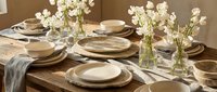 Elegant dining table setting with neutral tableware, white flowers in glass vases, and natural linen napkins for home entertaining and hospitality.