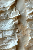 Crumpled white paper texture with dramatic shadows and folds creating abstract relief pattern. Natural light reveals subtle cream and beige tones in wrinkled surface.