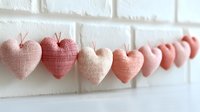 Handmade fabric hearts in pink tones hanging on string against white brick wall, romantic decoration for Valentine's Day, wedding or home decor projects.