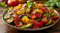 Colorful grilled vegetables with zucchini, bell peppers, tomatoes and fresh herbs on rustic plate, drizzled with balsamic glaze and seasoned with black pepper.