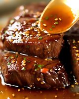 Juicy beef steak glazed with sweet and savory sauce, garnished with sesame seeds and fresh herbs for gourmet cooking.