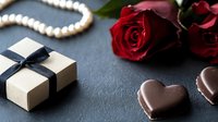 Romantic composition with heart shaped chocolates, red roses, pearl necklace and gift box with blue ribbon on dark stone background. Perfect for Valentine's Day designs.