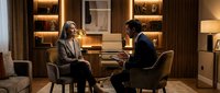Professional business meeting between confident businesswoman and businessman in modern luxury office with warm lighting and contemporary furniture.