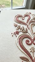 Elegant embroidered hearts and floral motifs in burgundy and brown threads on cream fabric showcasing traditional needlework craftsmanship and textile artistry.