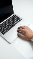 Man's hand with watch and ring using laptop trackpad on white desk, close-up view of working professional with modern computer.