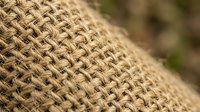 Close-up macro shot of natural burlap fabric texture showing detailed woven jute fibers in beige and brown tones for rustic crafting and packaging projects.
