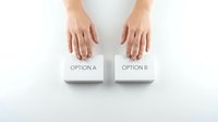 Female hands hovering over two white paper cards labeled option A and option B on clean white surface representing choice and decision making process.