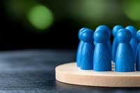 Blue wooden figures standing together on round wooden base against dark background with green bokeh, symbolizing teamwork and unity.