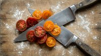 Fresh tomato slices arranged with chef knives on wooden cutting board dusted with flour, suitable for cooking, recipe, and food preparation content.
