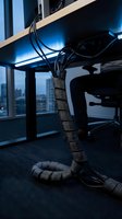 Modern office cable management system with organized wires wrapped in protective sleeves under standing desk in corporate workspace for productivity solutions.