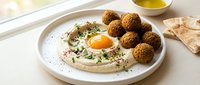Fresh homemade falafel balls served with creamy hummus, olive oil drizzle and herbs on white plate. Traditional Middle Eastern vegetarian meal with pita bread.