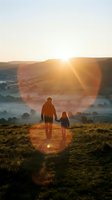 Adult woman and young child holding hands standing on hillside at sunrise overlooking misty valley landscape. Use for family, parenting, nature, and lifestyle content.