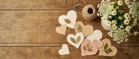 Handmade paper hearts with pressed flowers on rustic wooden background. Craft supplies and natural decorations for DIY projects and romantic gifts.