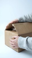 Person in light gray knit sweater opening brown cardboard box against white background, isolated for delivery and shipping concepts.