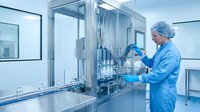 Pharmaceutical technician in sterile cleanroom operating automated filling equipment for drug manufacturing in modern laboratory facility.