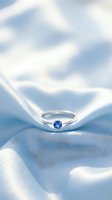 Elegant solitaire engagement ring with blue sapphire gemstone resting on white silk fabric, showcasing luxury jewelry design for weddings and special occasions.
