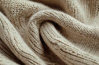 Soft beige knitted wool fabric with gentle folds and texture creates cozy winter background pattern, macro close up view showing detailed textile structure.